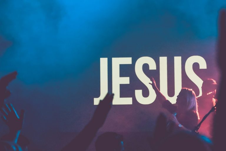 Worship crowd with hands raised beneath a JESUS sign